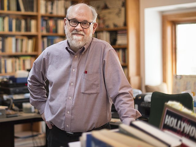 Portrait of David Bordwell standing in an office filled with books